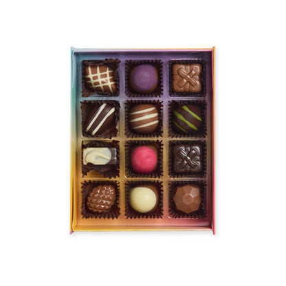 “Open rainbow chocolate box containing 12 assorted decorated chocolates arranged in four rows of three.”
