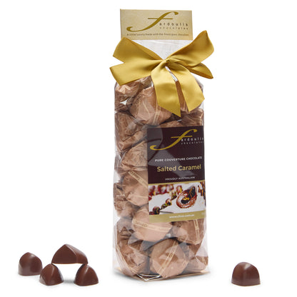 “Fardoulis salted caramel chocolates in a clear gift bag tied with a gold satin bow, with loose chocolates beside it.”